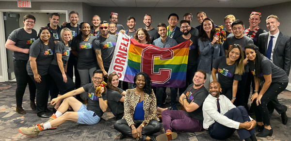 A large group poses with a Cornell rainbow flag