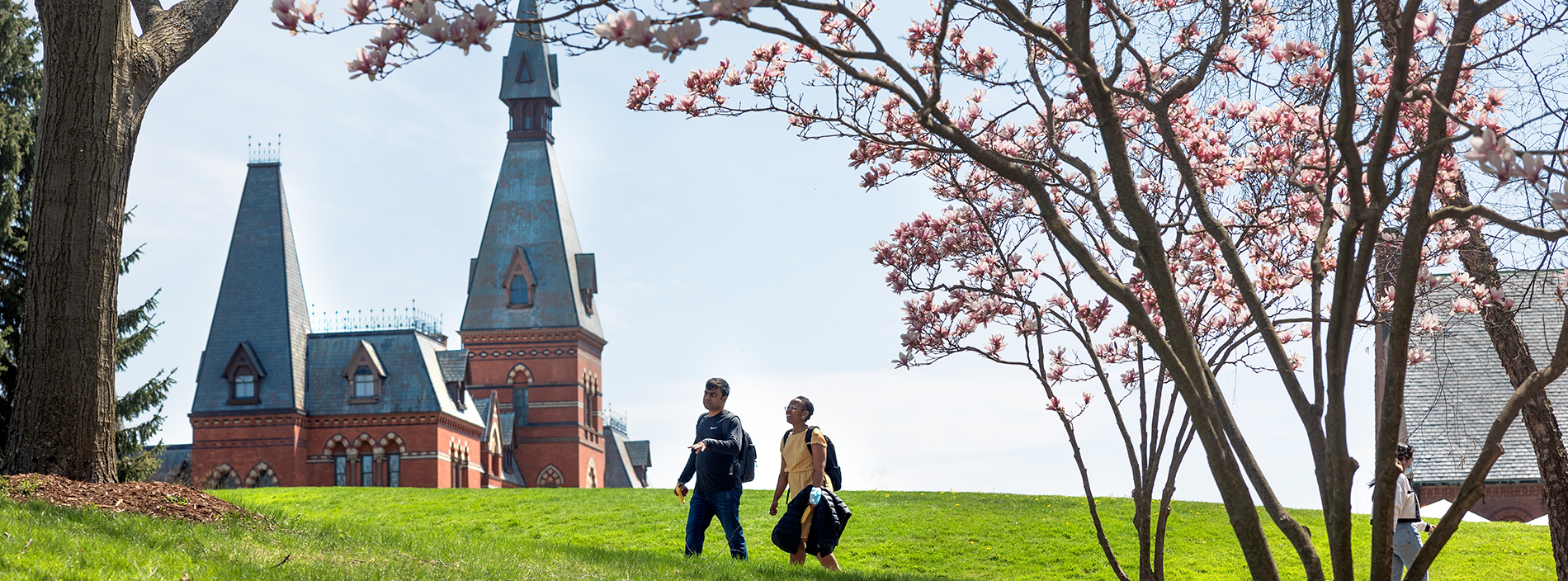 Two people walking across green grass with Sage Hall in the background.